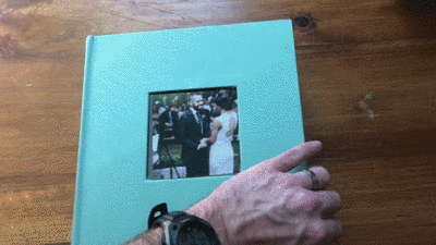 Animated GIF showing a cloth covered photo album with wedding photos inside.