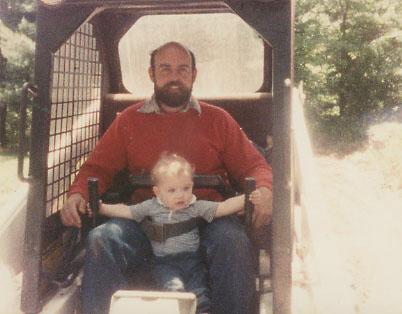 1980s photo of a dad and his son in a bobcat skid steer.