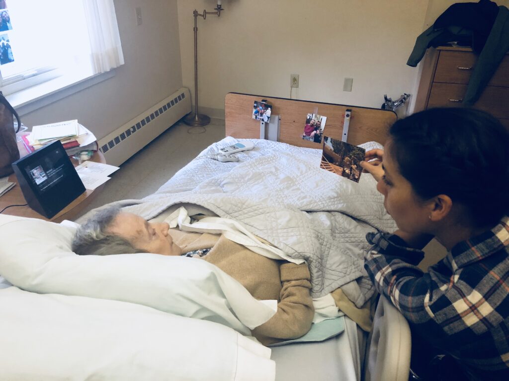 A grandmother in a hospital bed looking at photos with her daughter-in-law.