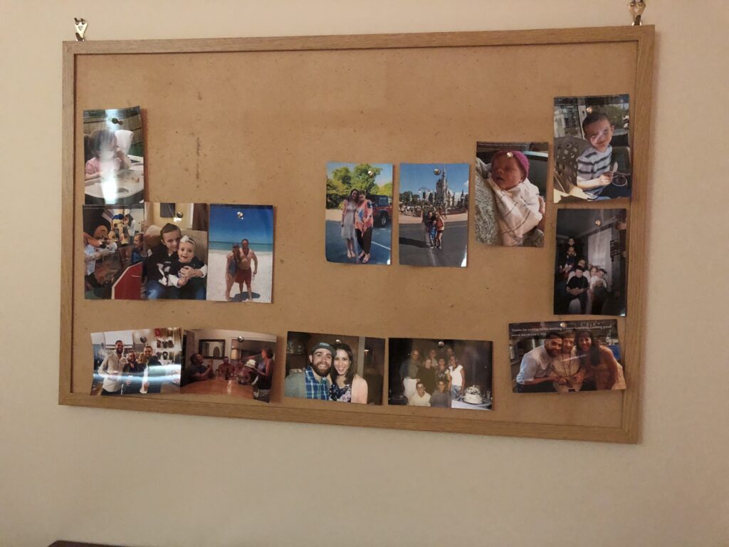 A cork board displaying several 4x6 photos printed and pinned on it. 