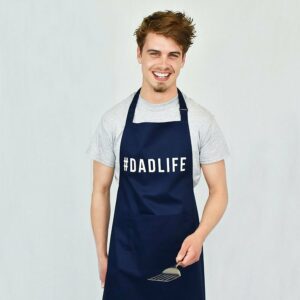 Young dad in a t-shirt wearing a blue apron reading "#DADLIFE"