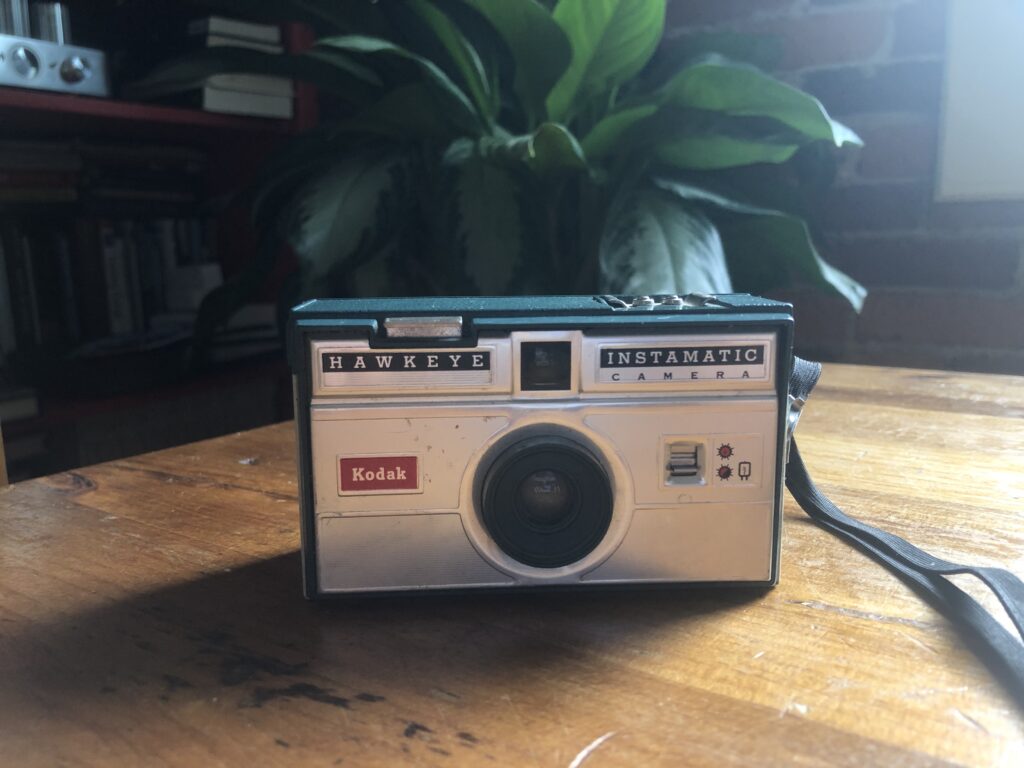 Photo of a Hawkeye Instamtic Camera from the 90s with a plant in the background.